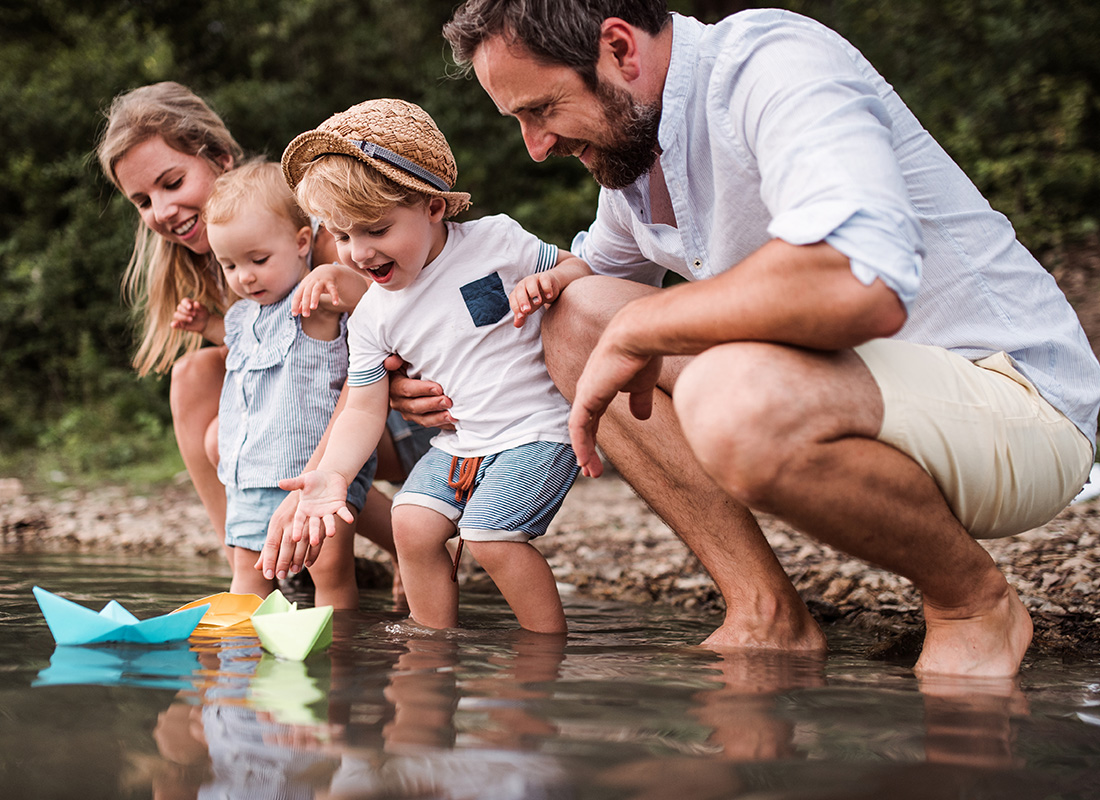Employee Benefits - Family and Their Young Children Place Paper Boats into a Lake